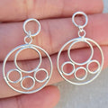 Silver circular earrings held between fingers against a neutral background