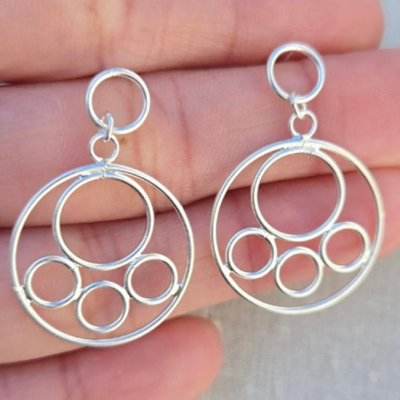 Silver circular earrings held between fingers against a neutral background