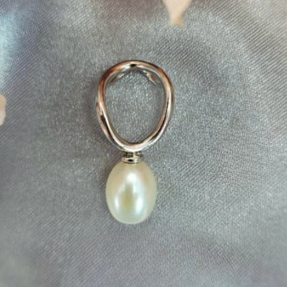 A silver pendant with a freshwater pearl attached to it, displayed on a fabric surface.