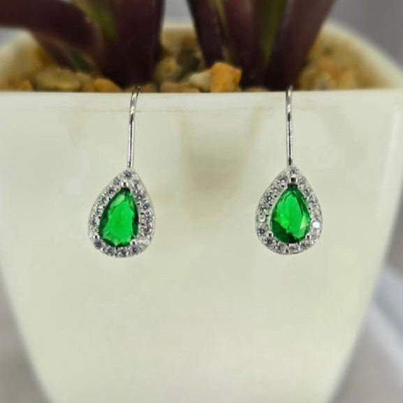 A pair of green cubic zirconia drop earrings with teardrop shape, set in sterling silver, displayed against a white floral background.