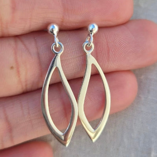 Silver earrings held between fingers against a neutral background