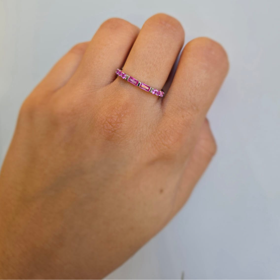 A hand wearing a sterling silver ring with a band of pink cubic zirconia.
