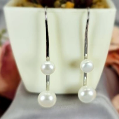 A pair of modern long silver earrings with three freshwater pearls, displayed in a white pot with a green plant.