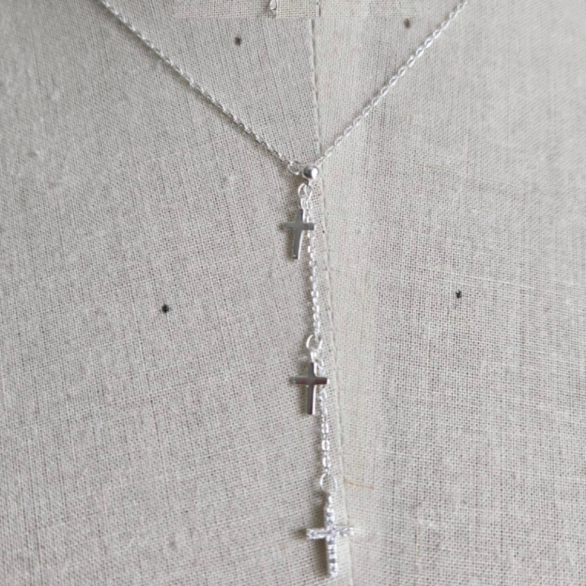 Silver cross necklace on a mannequin with a light gray background