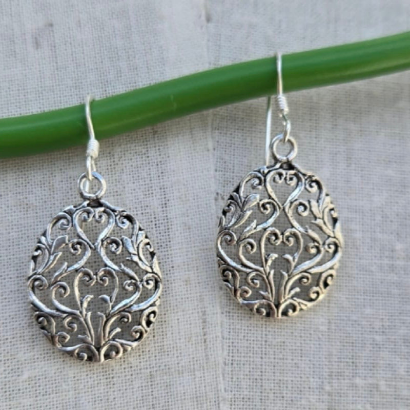 Silver filigree earrings on a textured fabric background