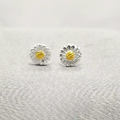 A pair of 7mm daisy stud earrings made of sterling silver, with a yellow detail in the center of each flower, displayed against a white background.