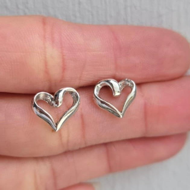 Silver heart-shaped earrings held between fingers on a neutral background
