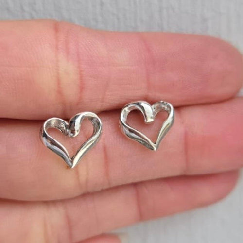 Silver heart-shaped earrings held between fingers on a neutral background