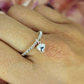 A sterling silver bobble ring with a dangling puffy heart charm, displayed on a person's hand.