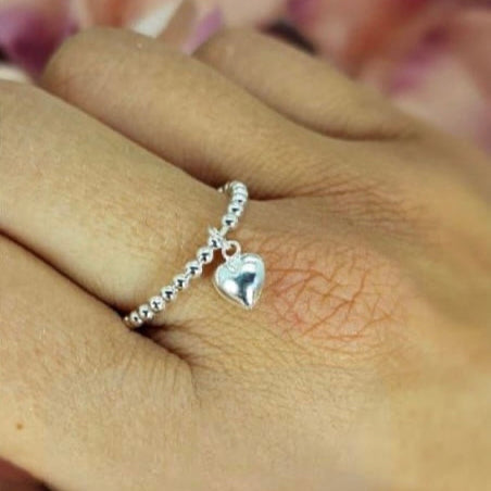 A sterling silver bobble ring with a dangling puffy heart charm, displayed on a person's hand.