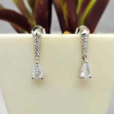 Silver hoop earrings with clear stones on a white surface with a plant in the background