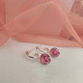 Silver hoop earrings with pink gemstones on a white surface with pink fabric in the background