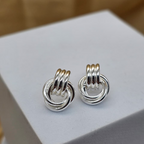 Pair of silver interlinked ring earrings on a white stand with a blurred background