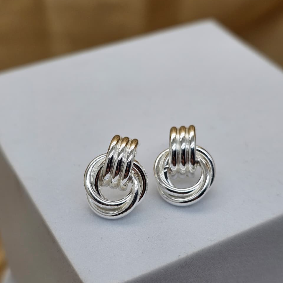 Pair of silver interlinked ring earrings on a white stand with a blurred background