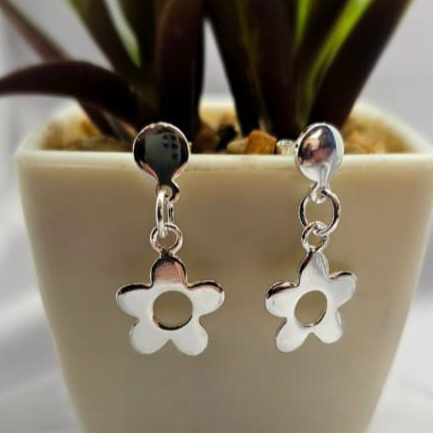 A pair of sterling silver stud earrings designed in the shape of daisies, displayed in a white vase with a green plant.