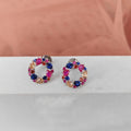 Multicolored circular earrings on a white surface with a pink fabric background