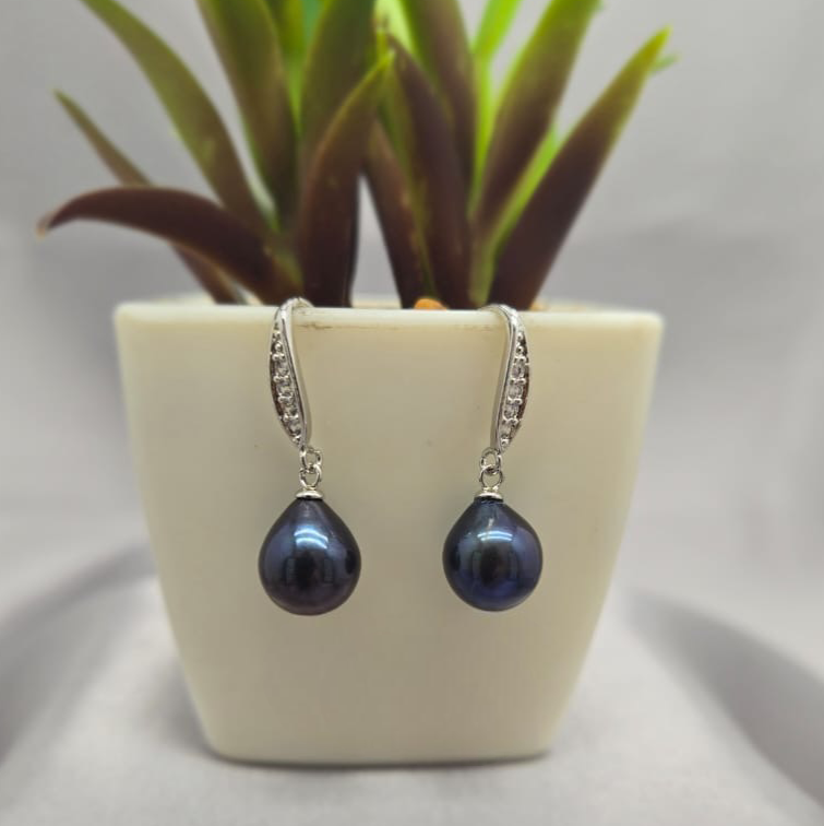 Pair of black pearl earrings on a white surface with a plant in the background