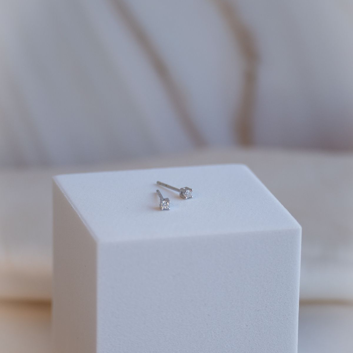 Pair of silver stud earrings on a white cube with a blurred background