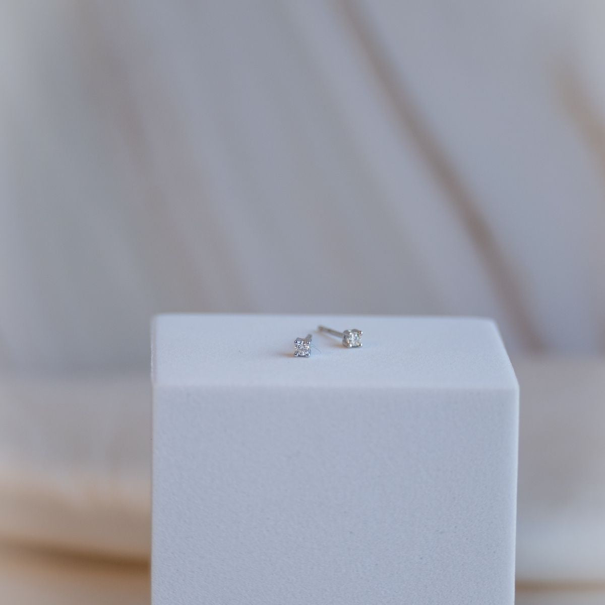 Pair of silver stud earrings on a white cube with a blurred background