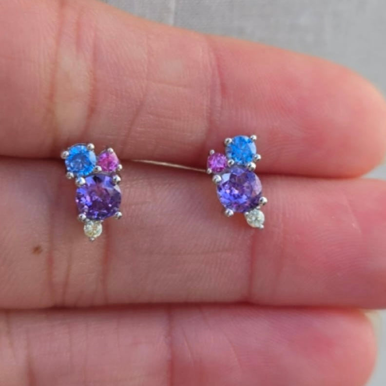 Pair of earrings with blue and purple gemstones held between fingers.
