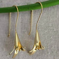 Gold flower-shaped earrings on a green stick against a gray background
