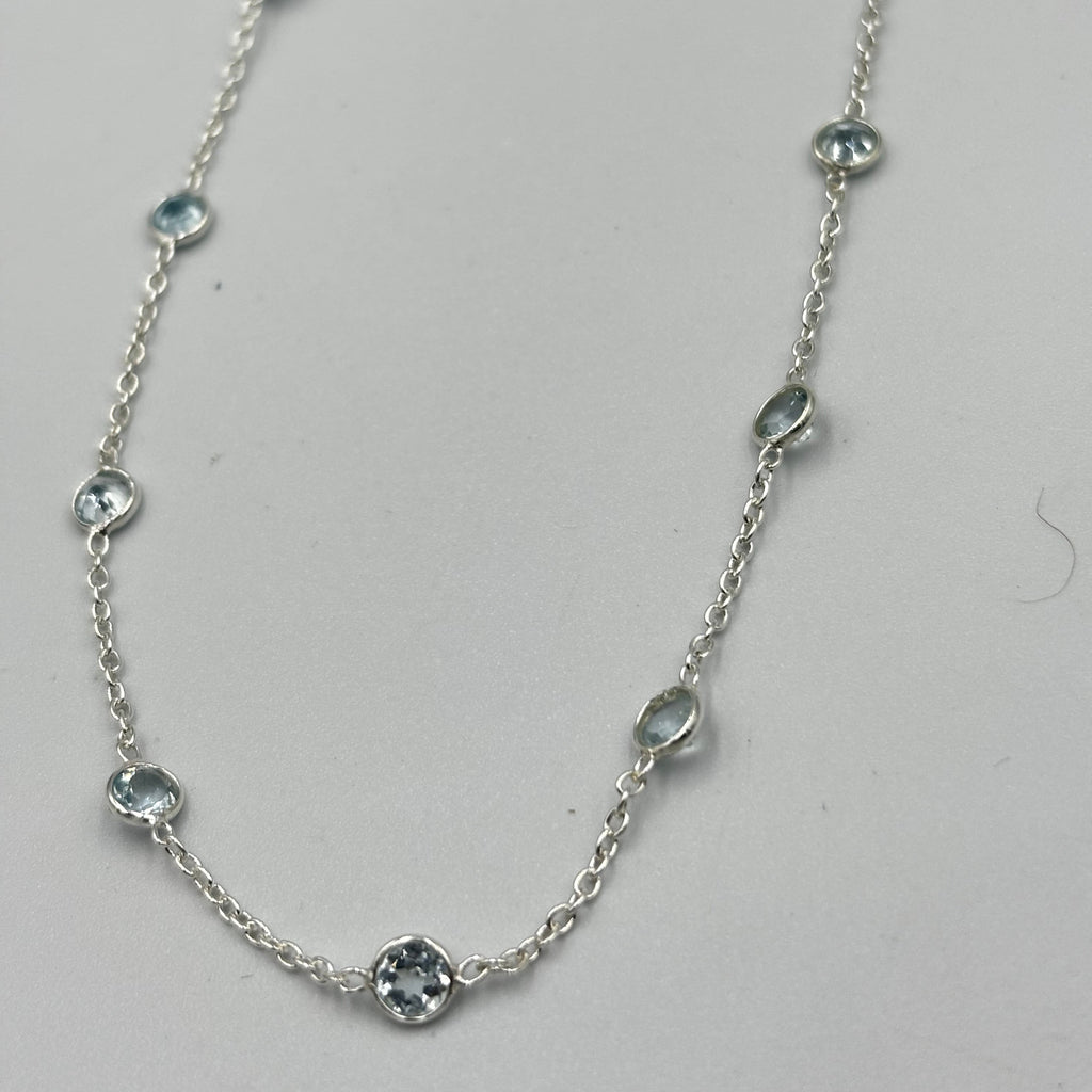 A sterling silver necklace with 5mm blue topaz semi-precious stones embedded in it, displayed against a white background.