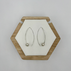 A pair of modern hook drop earrings with freshwater pearls displayed on a wooden hexagonal stand against a white background.
