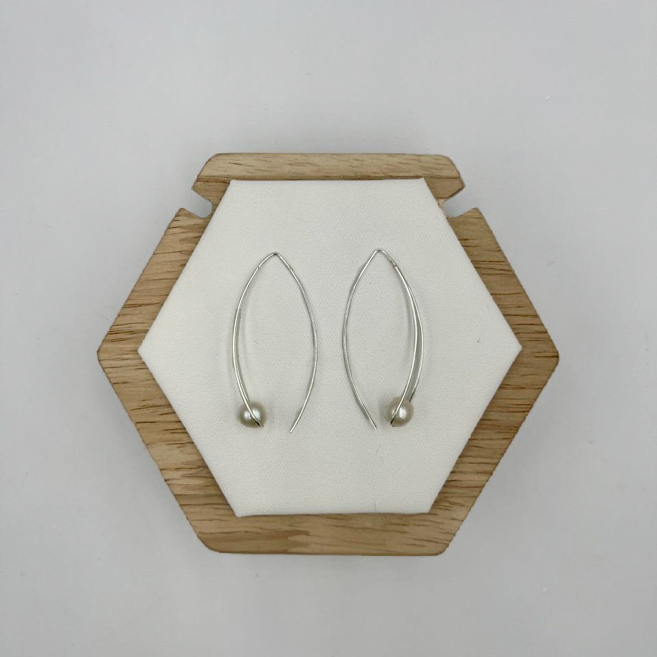 A pair of modern hook drop earrings with freshwater pearls displayed on a wooden hexagonal stand against a white background.