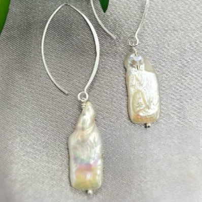 A pair of rectangular white freshwater pearl earrings with sterling silver hooks, displayed on a textured surface.