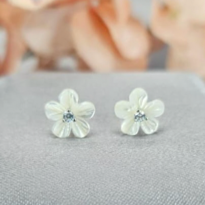 A pair of Mother of Pearl Daisy earrings with sterling silver studs and a central mother of pearl and cubic zirconia on a grey surface.