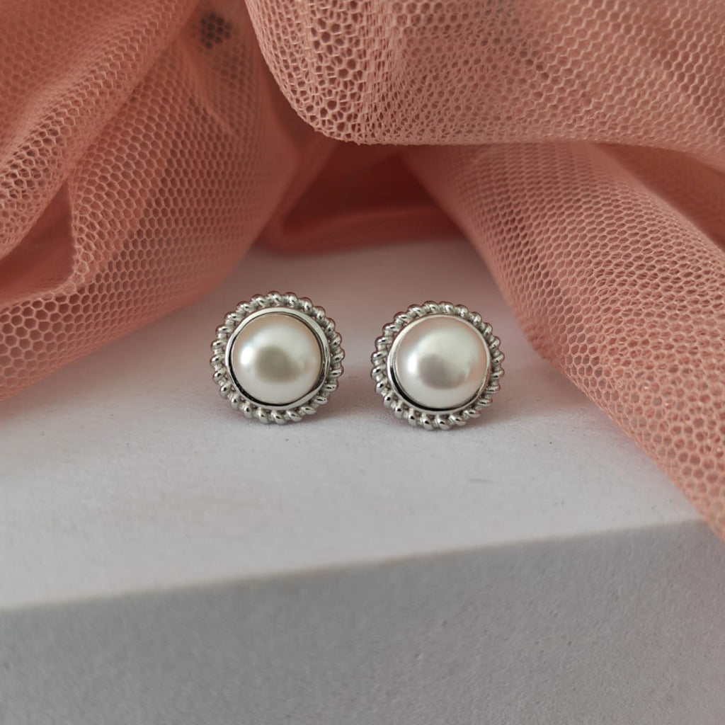 Pearl stud earrings on a light pink fabric background