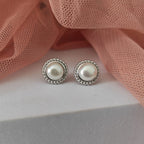 Pearl stud earrings on a light pink fabric background