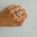 A sterling silver ring with a large square cubic zirconia and two round ones displayed on a person's hand.