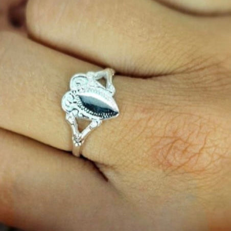 A sterling silver heart signet ring on a person's finger, with the ring's design visible on the top part of the finger.
