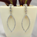Silver hoop earrings on a white surface with a plant in the background
