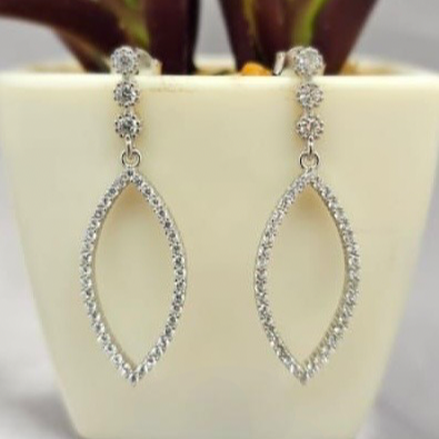 Silver hoop earrings on a white surface with a plant in the background