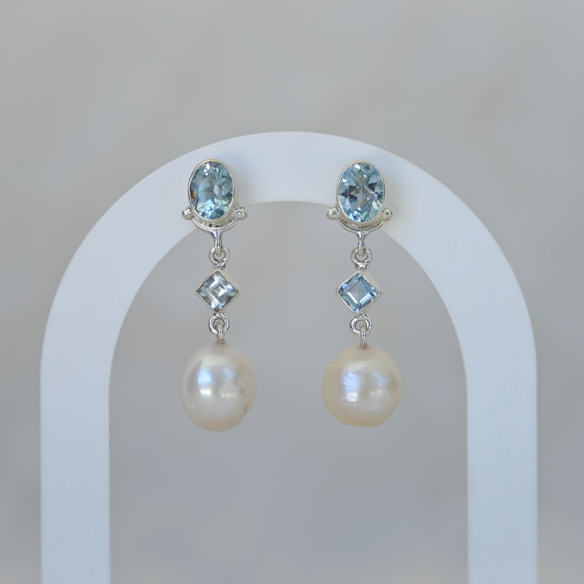 Pair of earrings with pearls and blue gemstones on a white arch background