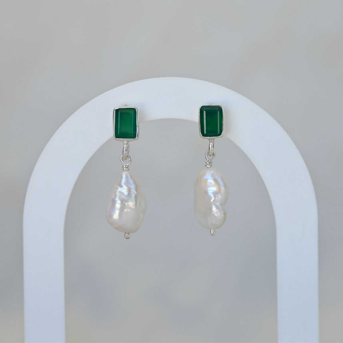 Pair of earrings with green square tops and pearl drops on a white arch background