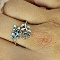 A sterling silver ring with an open size leaf design, displayed on a person's finger.
