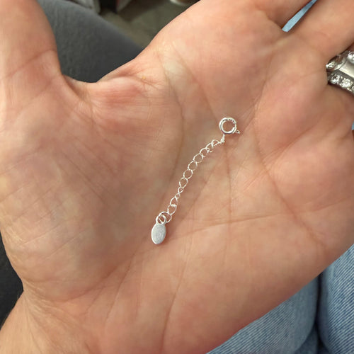 Silver chain necklace held in a hand with a blurred background