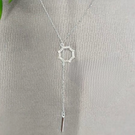 A sterling silver necklace with a bling circle and hanging chain detail displayed on a fabric surface.