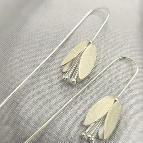 A pair of sterling silver drop earrings with a floral design, displayed against a textured grey background.