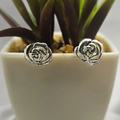 A pair of sterling silver rose-shaped stud earrings in a white pot with a green plant.