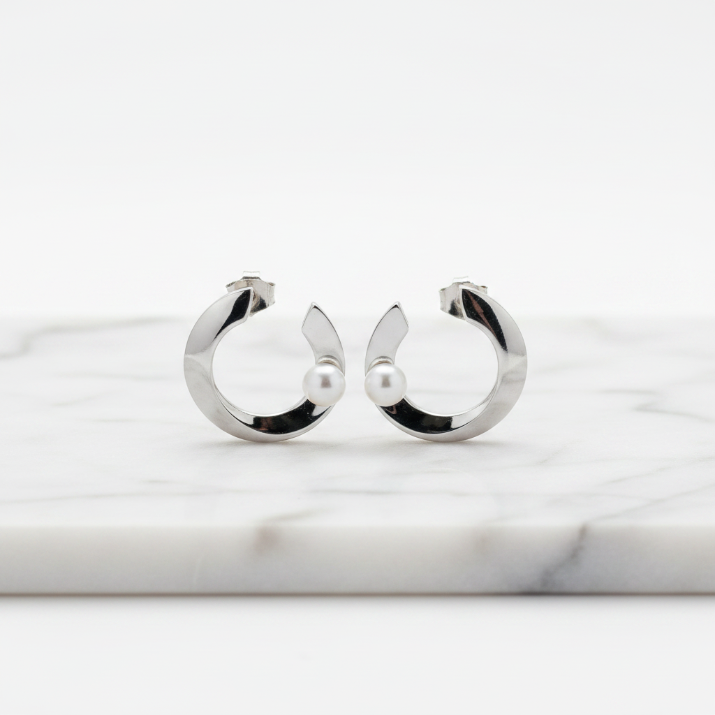 C-shaped sterling silver earrings with a central freshwater pearl, displayed in a white vase with a green plant.