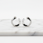 C-shaped sterling silver earrings with a central freshwater pearl, displayed in a white vase with a green plant.