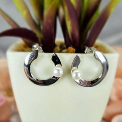 C-shaped sterling silver earrings with a central freshwater pearl, displayed in a white vase with a green plant.