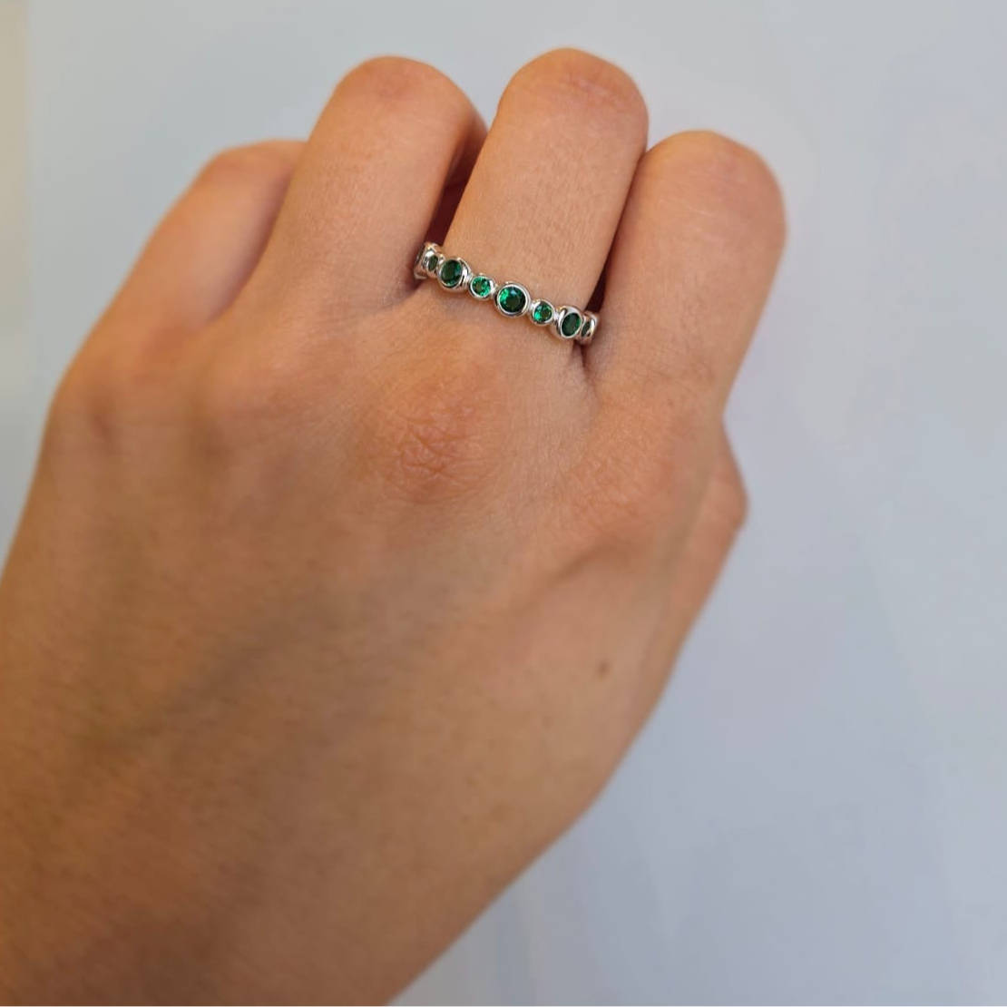 A hand wearing a green cubic zirconia stacking ring with a silver band.
