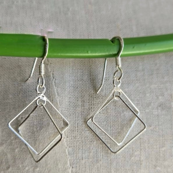 Silver square hoop earrings hanging on a green rod against a gray background