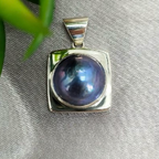 A blue Mabe Pearl pendant with a sterling silver setting, displayed against a fabric background.