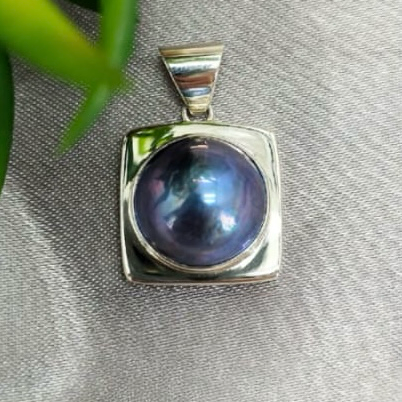 A blue Mabe Pearl pendant with a sterling silver setting, displayed against a fabric background.